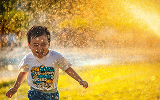 Asian male child running through a sprinkler on a sunny day