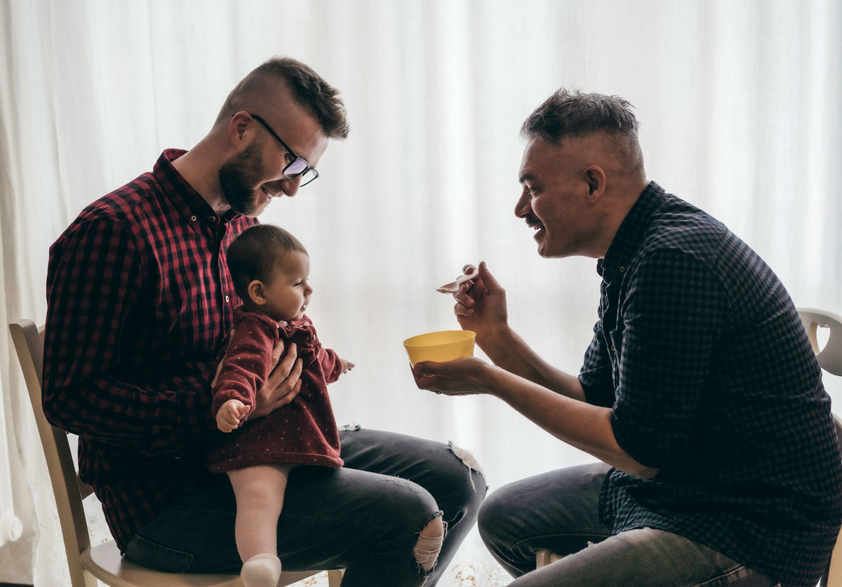 Two men feeding a baby